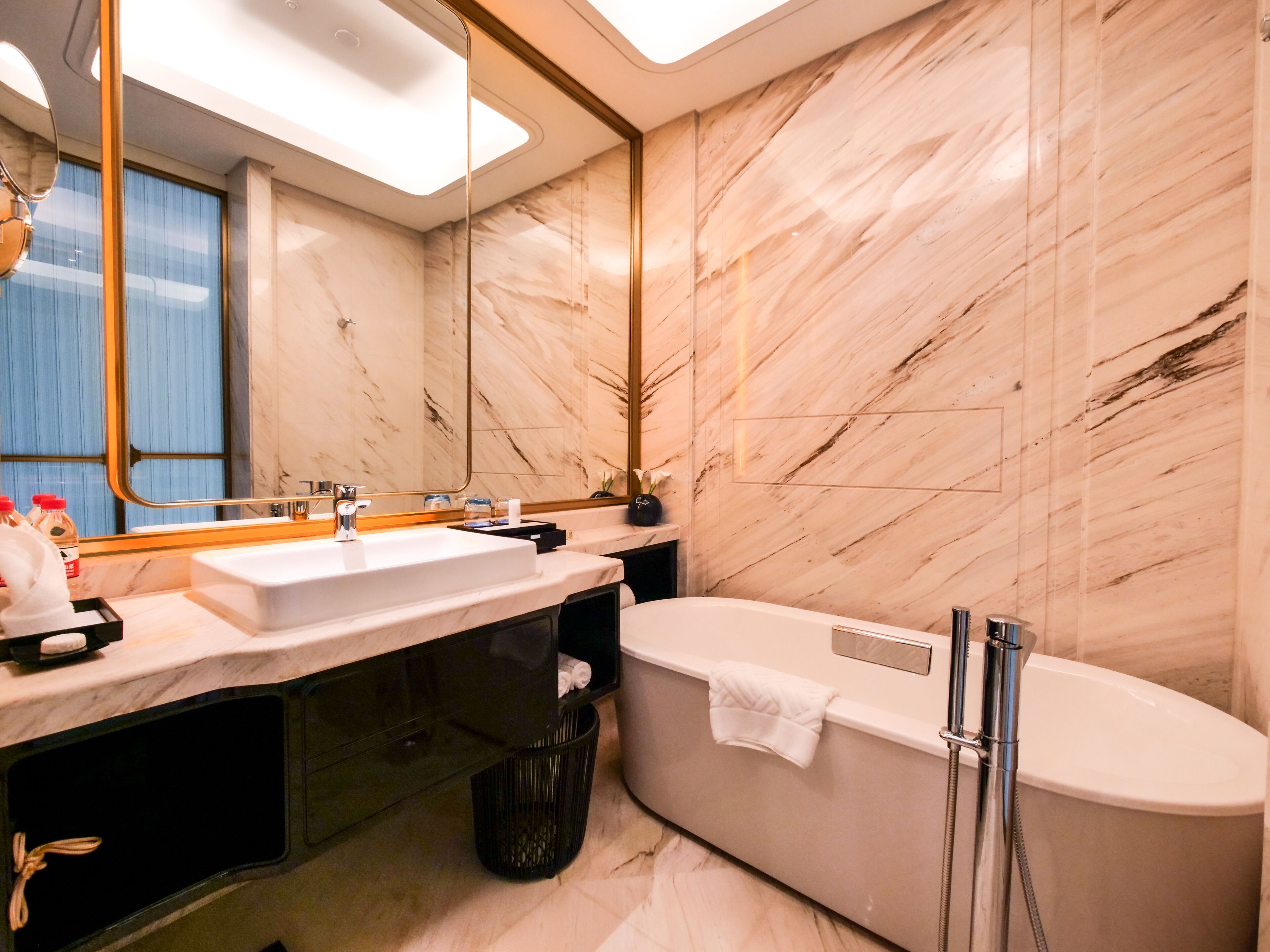 Un baño moderno con un espejo grande, dos lavamanos, una bañera y paredes de mármol.