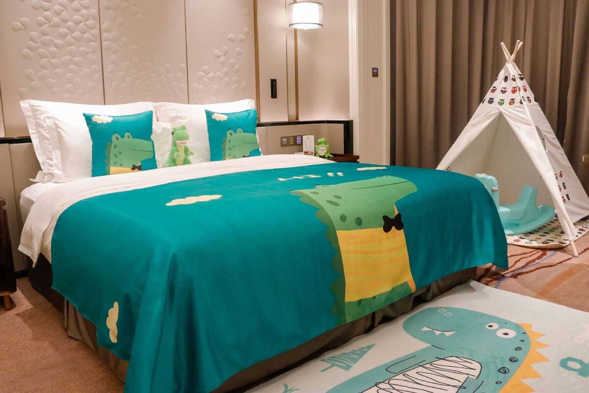 Habitación de hotel con cama, mesita de noche, lámpara, un tipi y una alfombra con temática de dibujos animados.