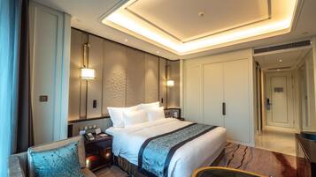 A modern hotel room with a large bed, a seating area with a sofa and armchair, a small table, and a mirror.