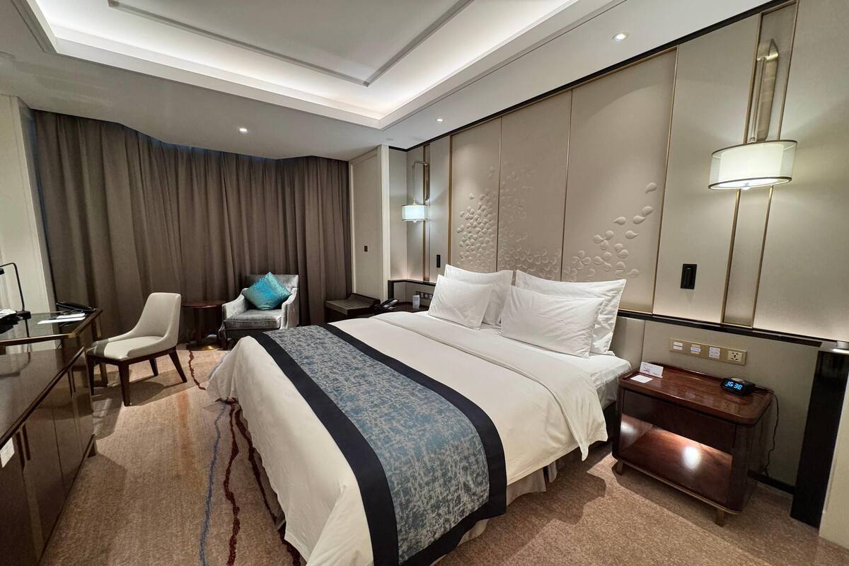 Una habitación de hotel con una cama grande, un escritorio, una silla, una mesita de noche y una lámpara.
