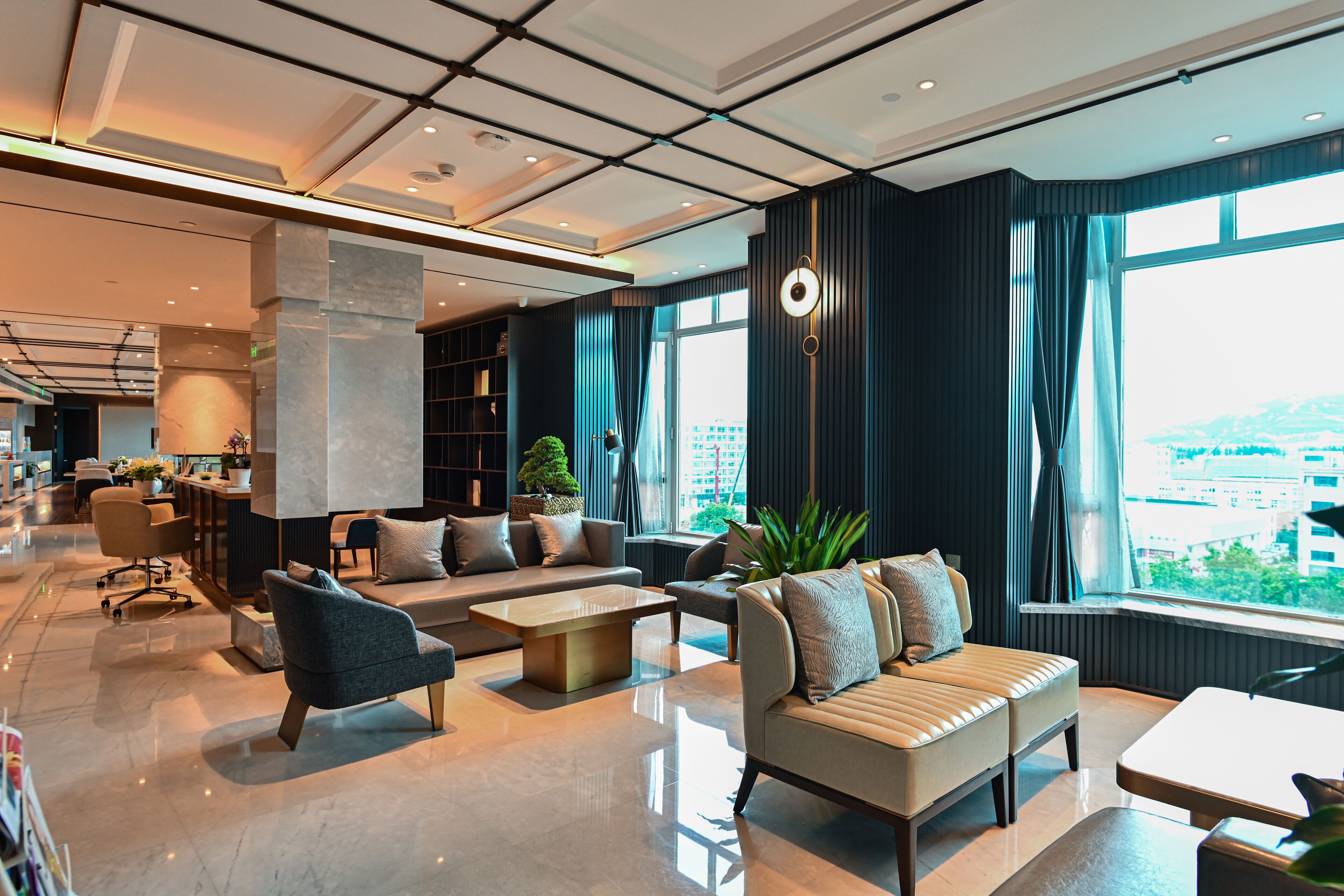 A modern hotel lobby with a spacious seating area, a coffee table, and a large window offering a city view.