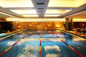 A large indoor swimming pool with lane dividers, a ceiling with recessed lighting, and a seating area with tables and chairs. - Wyndham Qingdao (Qingdao)