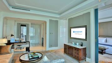 Una habitación de hotel moderna con un televisor de pantalla plana grande, una zona de estar cómoda con un sofá y un sillón, un mueble de madera y un espejo grande.
