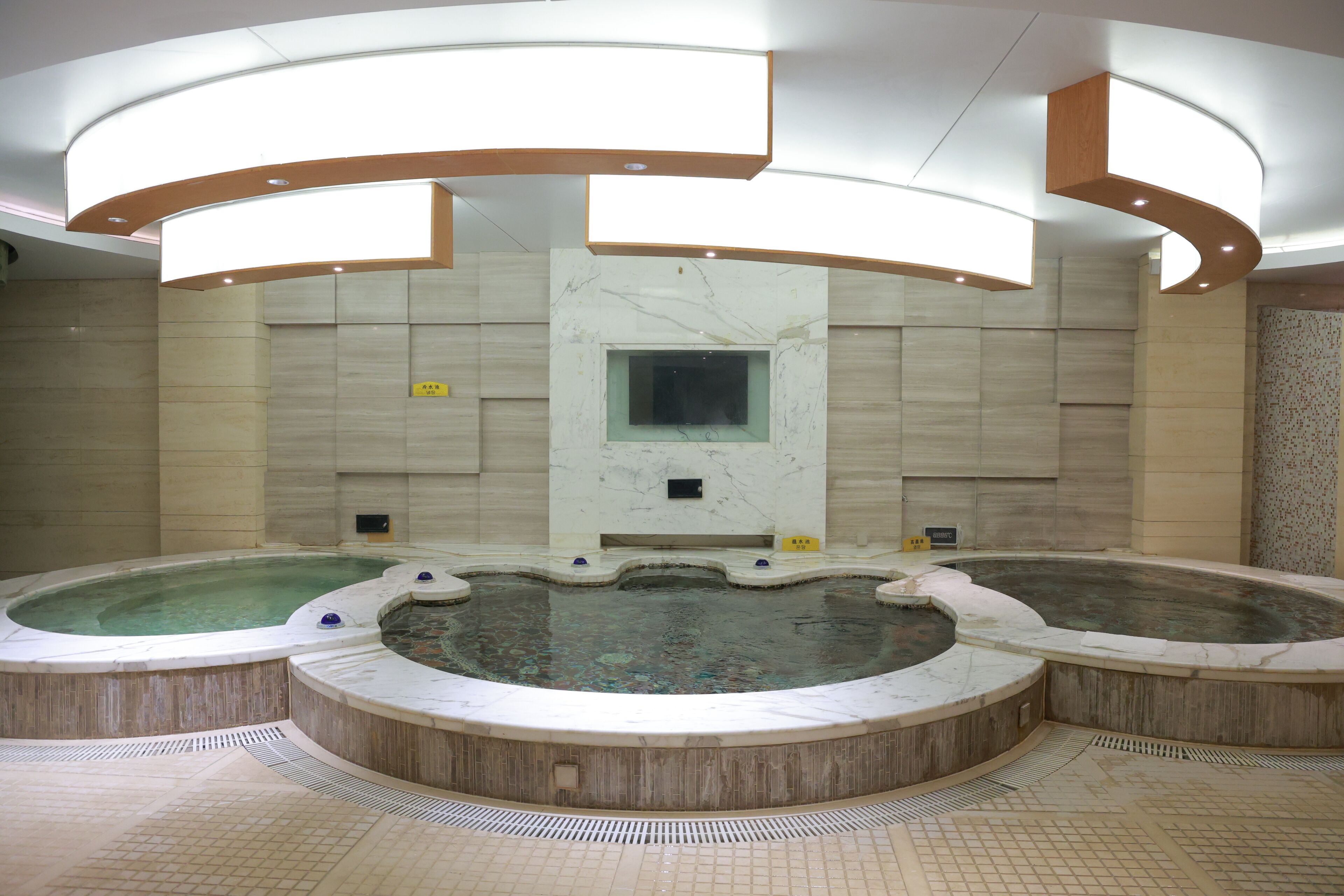 A large indoor swimming pool with multiple hot tubs, a central viewing window, and a tiled floor.