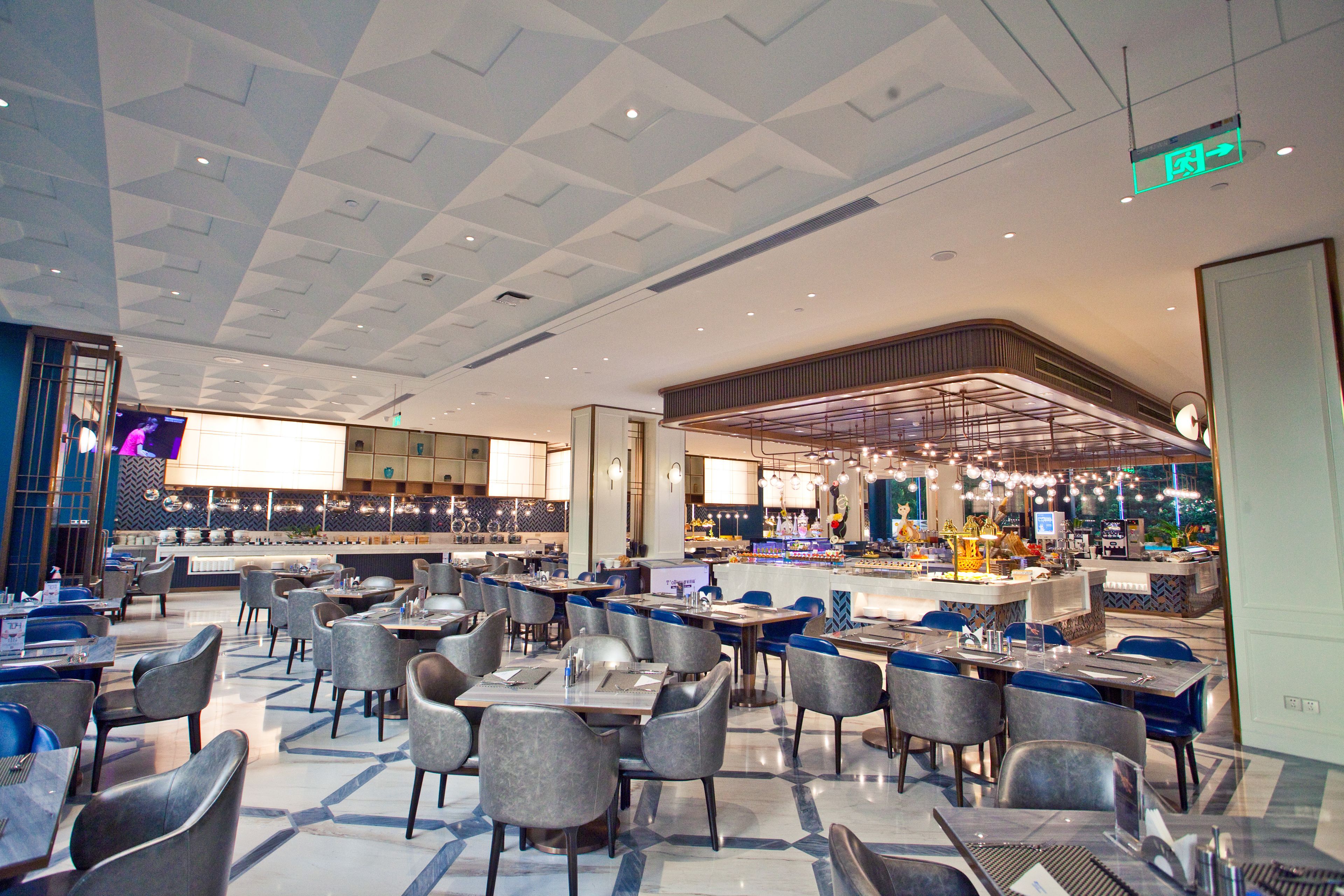 Un restaurant spacieux doté d’un plafond au design moderne, de nombreuses tables et chaises, et d’un bar central.