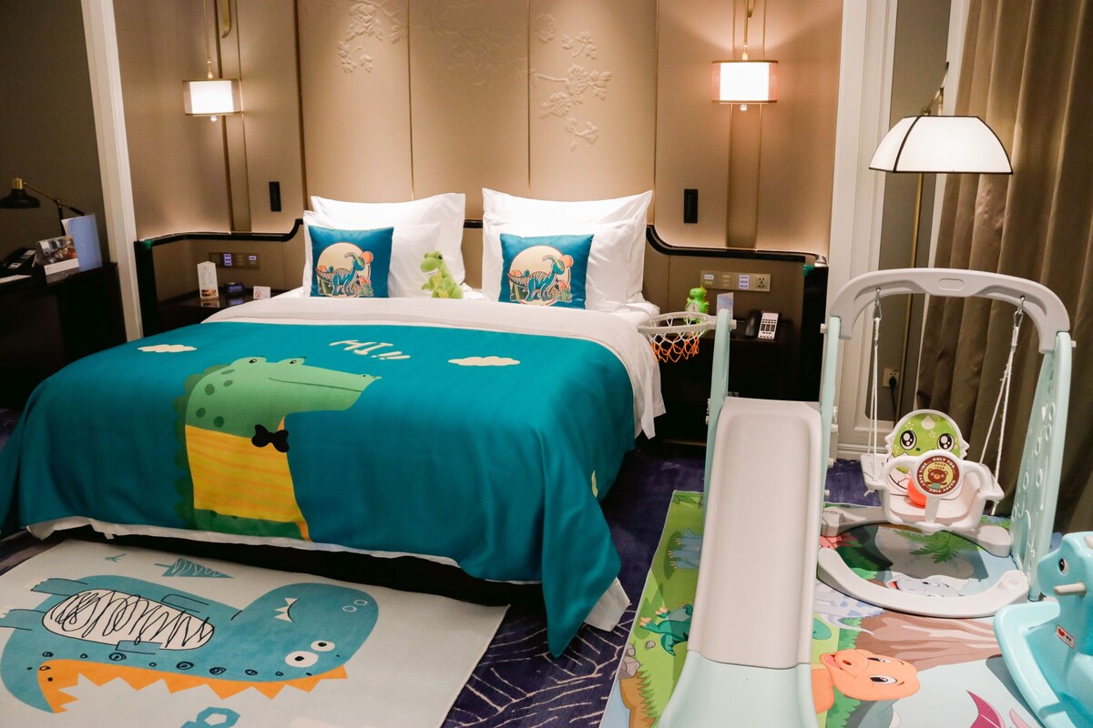 Una habitación de hotel con cama, mesita de noche, escritorio, silla y cuna.