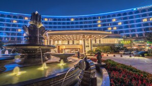 Un hotel con una fuente circular, un edificio moderno con iluminación azul y un cartel de Wyndham.