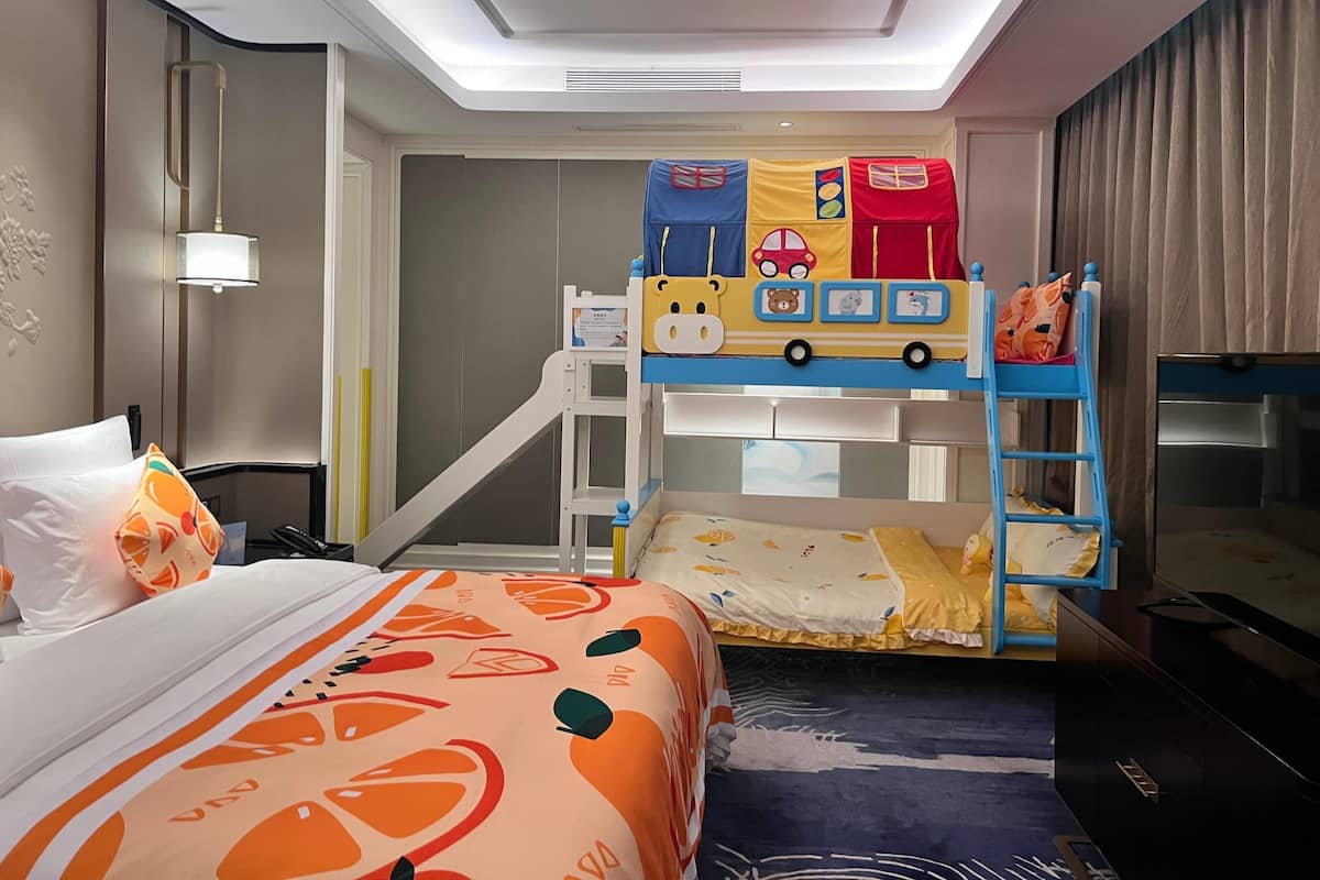 Habitación de hotel con literas, un escritorio, una silla, un televisor y una cama con colcha estampada.