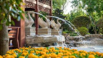Ein traditionelles Pavillon mit einer Steintreppe und Wasserspeiern, umgeben von einem Garten mit Studentenblumen.