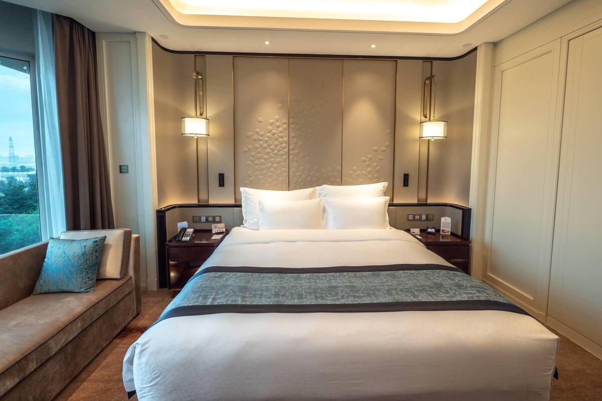 Habitación de hotel con una cama grande, mesitas de noche, un sofá y vistas al exterior.