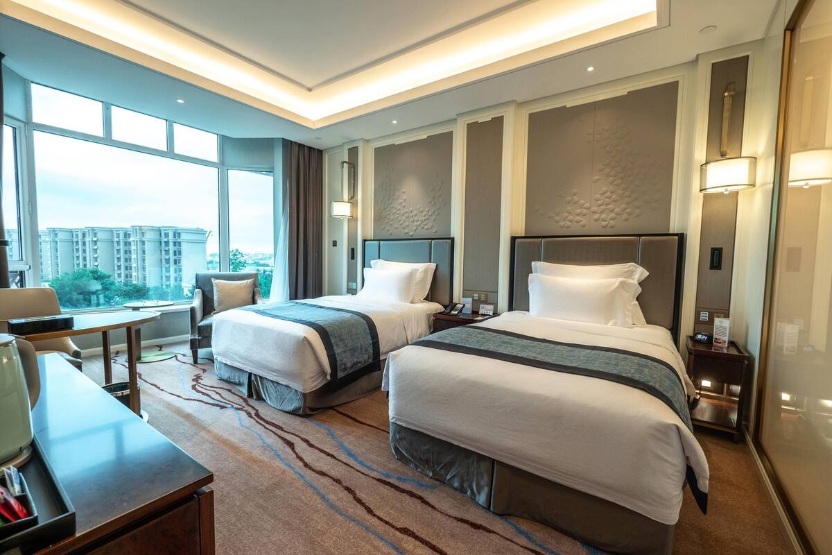 Habitación de hotel con dos camas, un escritorio y vistas a la ciudad.