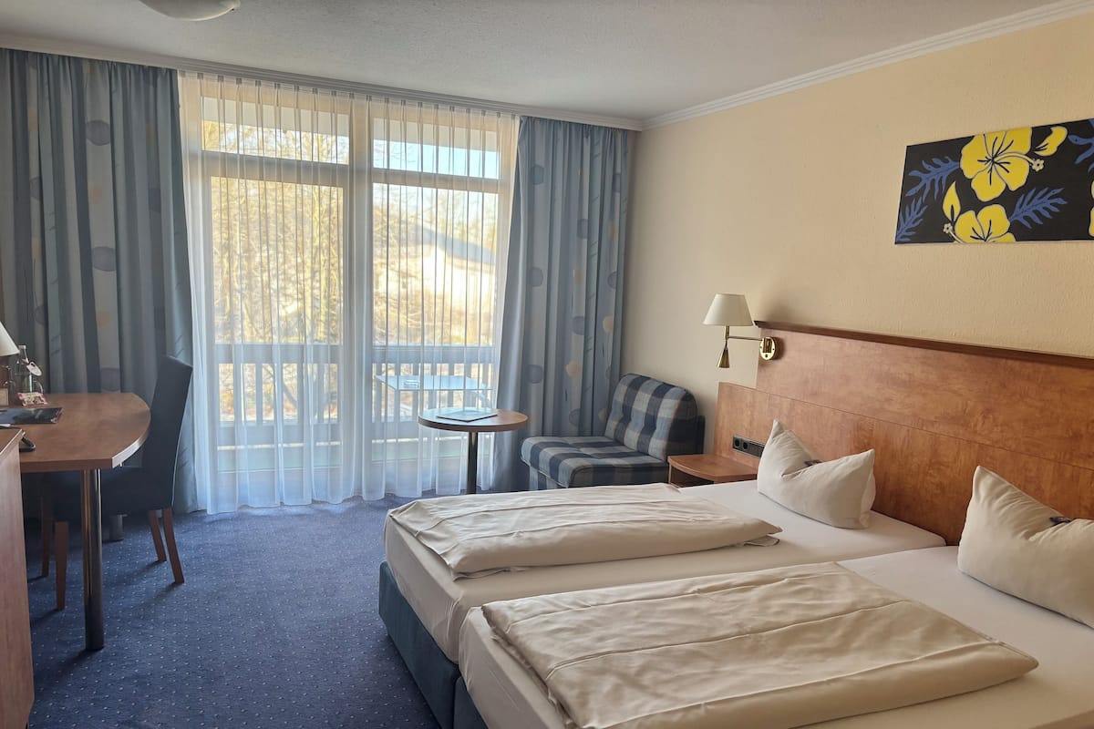 A hotel room with two beds, a desk, a chair, a small table, and a window with curtains.