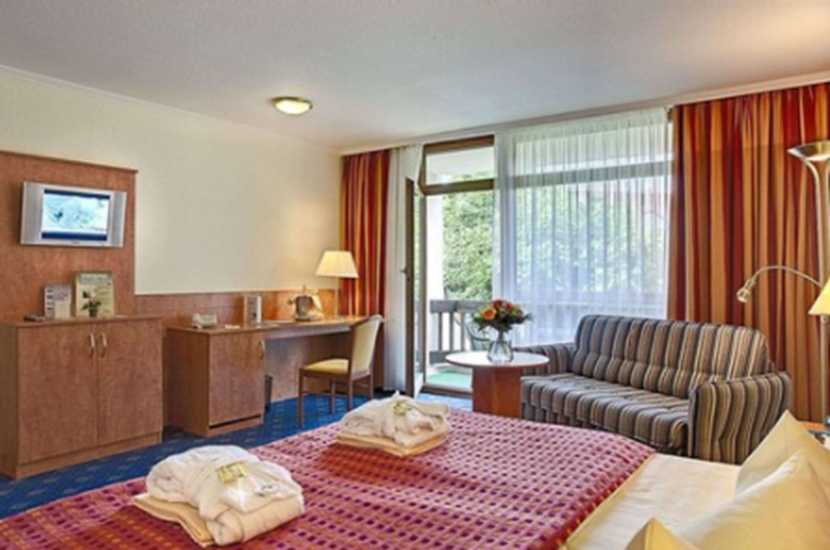 A hotel room with a bed, a desk, a chair, a sofa, and a small table with a vase of flowers.