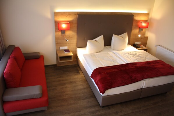 Una habitación de hotel con una cama, un sofá rojo y dos lámparas de noche.