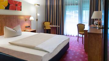 Une chambre d’hôtel avec un grand lit, un bureau, une chaise, une lampe et une fenêtre avec des rideaux.