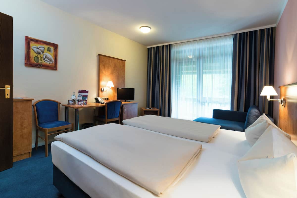 A hotel room with two beds, a desk with a computer, a chair, a television, and a painting on the wall.