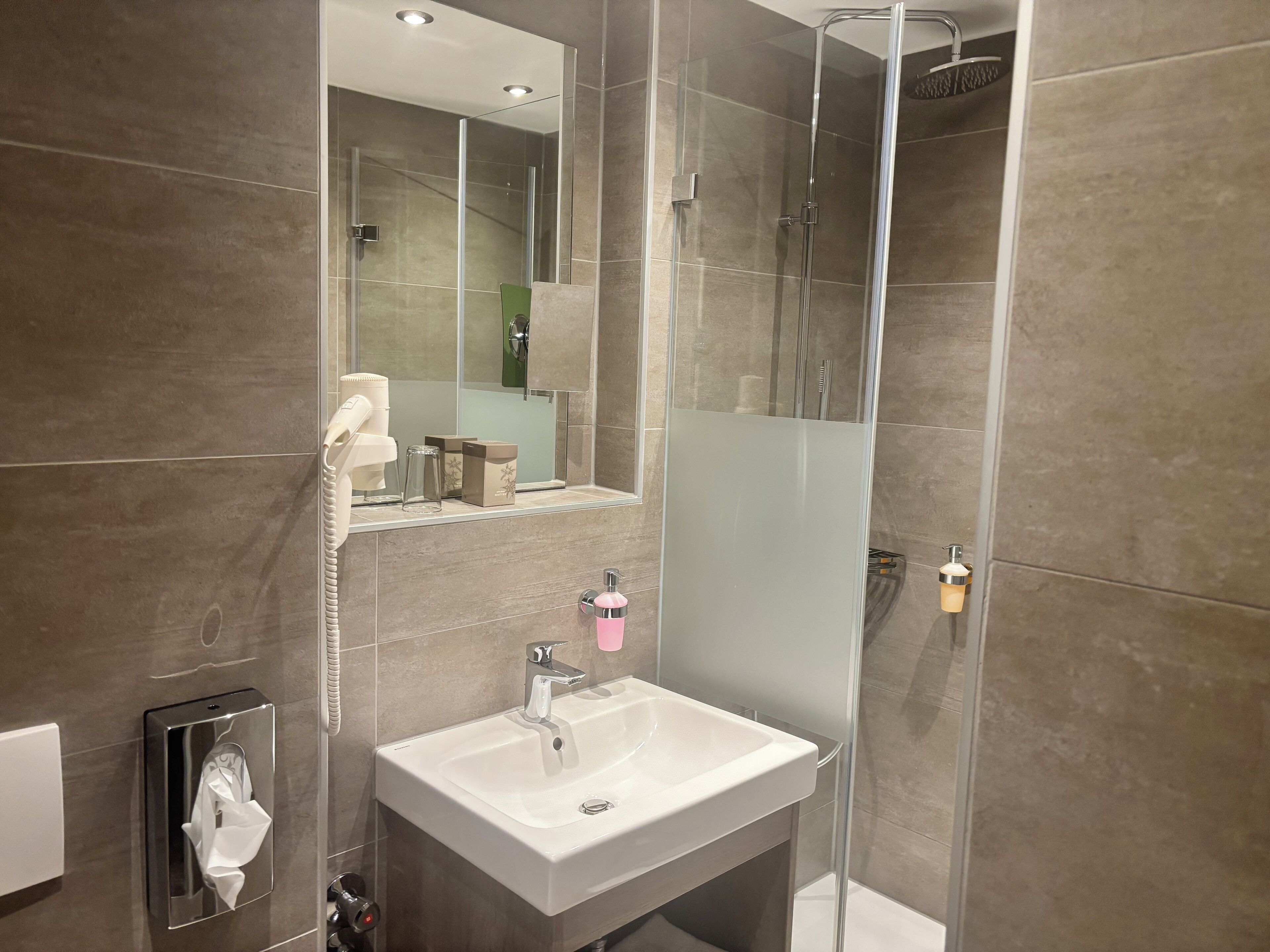 A modern bathroom with a glass-enclosed shower, a white sink, and a mirror above the sink.