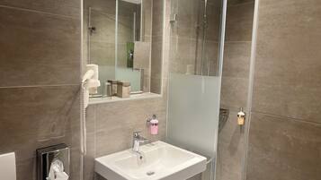 Un baño moderno con cabina de ducha de vidrio, un lavabo blanco y un espejo sobre él.