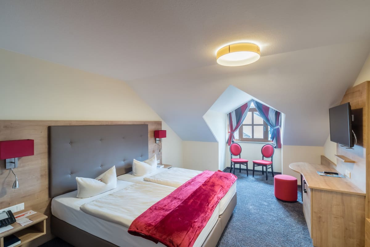 A hotel room with a large bed, a desk, a TV, and a view of the outside.