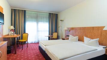 Ein Hotelzimmer mit zwei Betten, einem Schreibtisch mit Lampe, einem Sessel und einem kleinen Tisch.