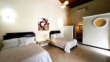 A hotel room with two beds, a small table, a wall-mounted artwork, a mirror, and a unique circular window.