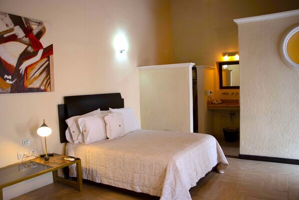 A bedroom with a bed, bedside table, lamp, and a painting on the wall. - Casa Padua (Puebla)