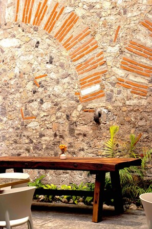 A rustic stone wall with brick patterns, a wooden table, and potted plants. - Casa Padua (Puebla)