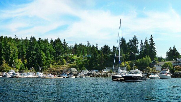 A marina with boats docked, surrounded by dense forest and a large building in the background. - The Lund Resort at Klah ah men (Lund)
