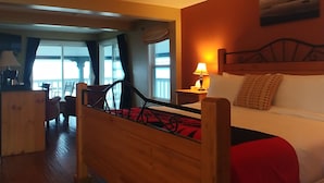A hotel room with a wooden bed, a white sofa, a nightstand with a lamp, and a view of the balcony through the window. - The Lund Resort at Klah ah men (Lund)