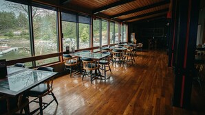A restaurant with wooden floors and large windows offering a view of a river and trees. - The Lund Resort at Klah ah men (Lund)
