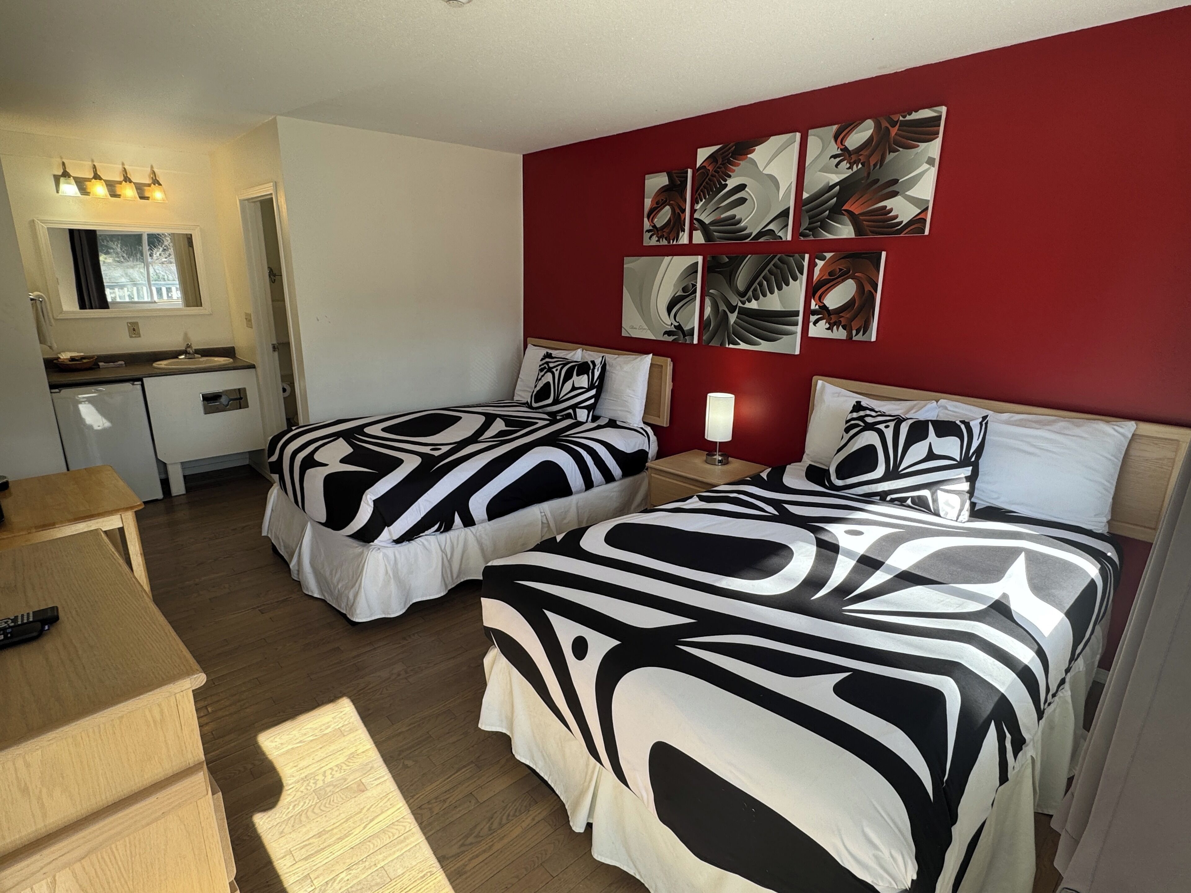 Camera d'albergo con due letti, un angolo cottura e una parete rossa decorata con opere d'arte.