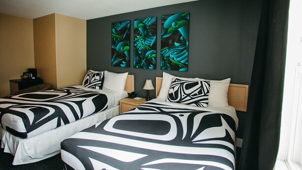 A hotel room with two beds, each with a black and white patterned bedspread. There are two wall-mounted paintings above the beds, and a small bedside table with a lamp and a phone. - The Lund Resort at Klah ah men (Lund)