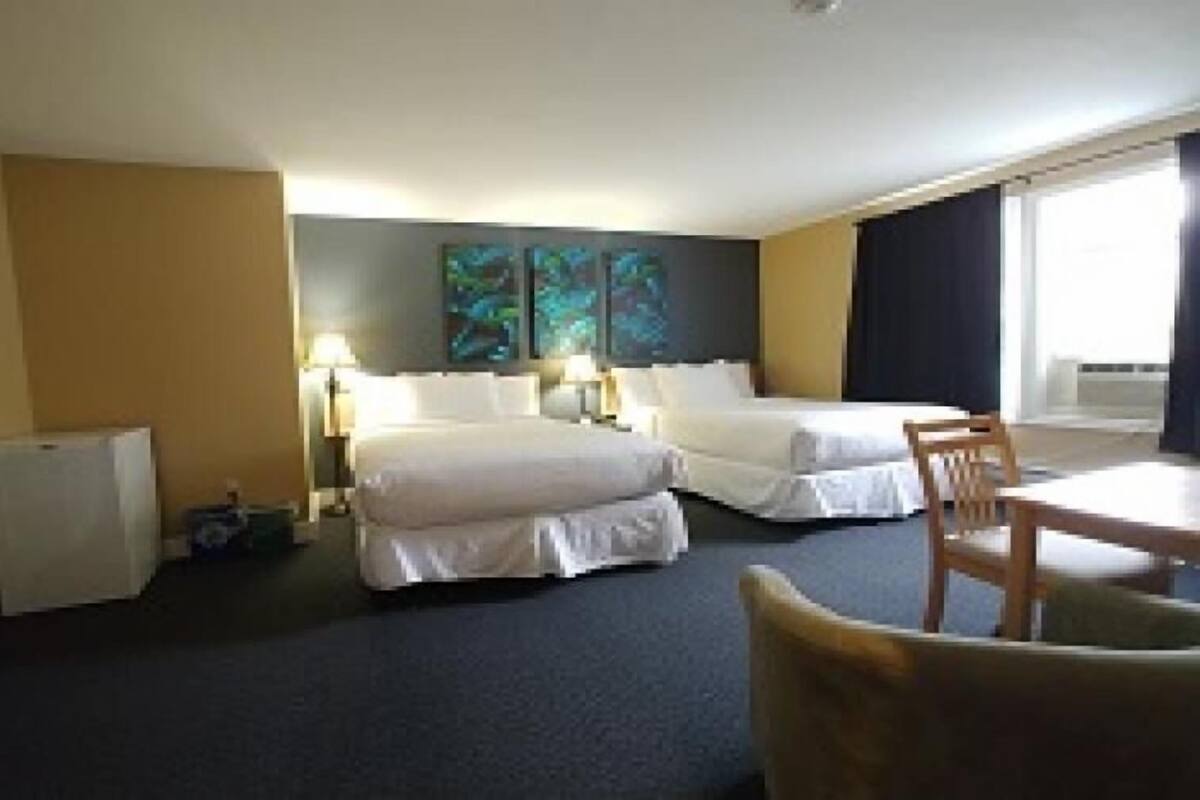 Habitación de hotel con dos camas, un escritorio, una silla, una lámpara y un refrigerador pequeño.