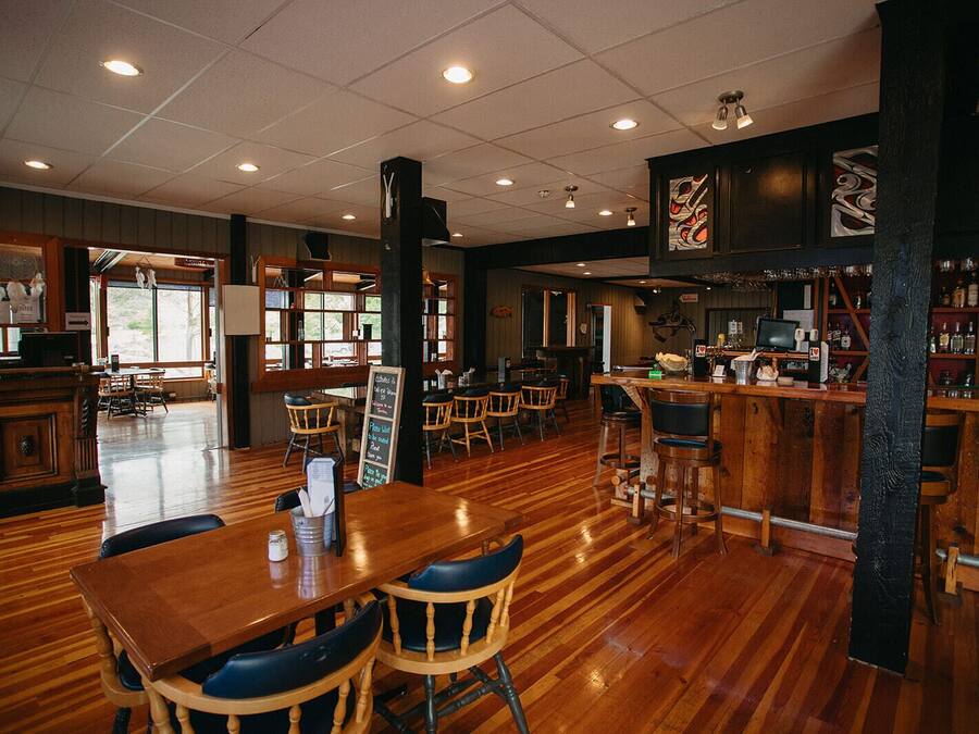 Amplia zona de bar con suelo de madera, diversos arreglos de asientos y una barra con distintos artículos.