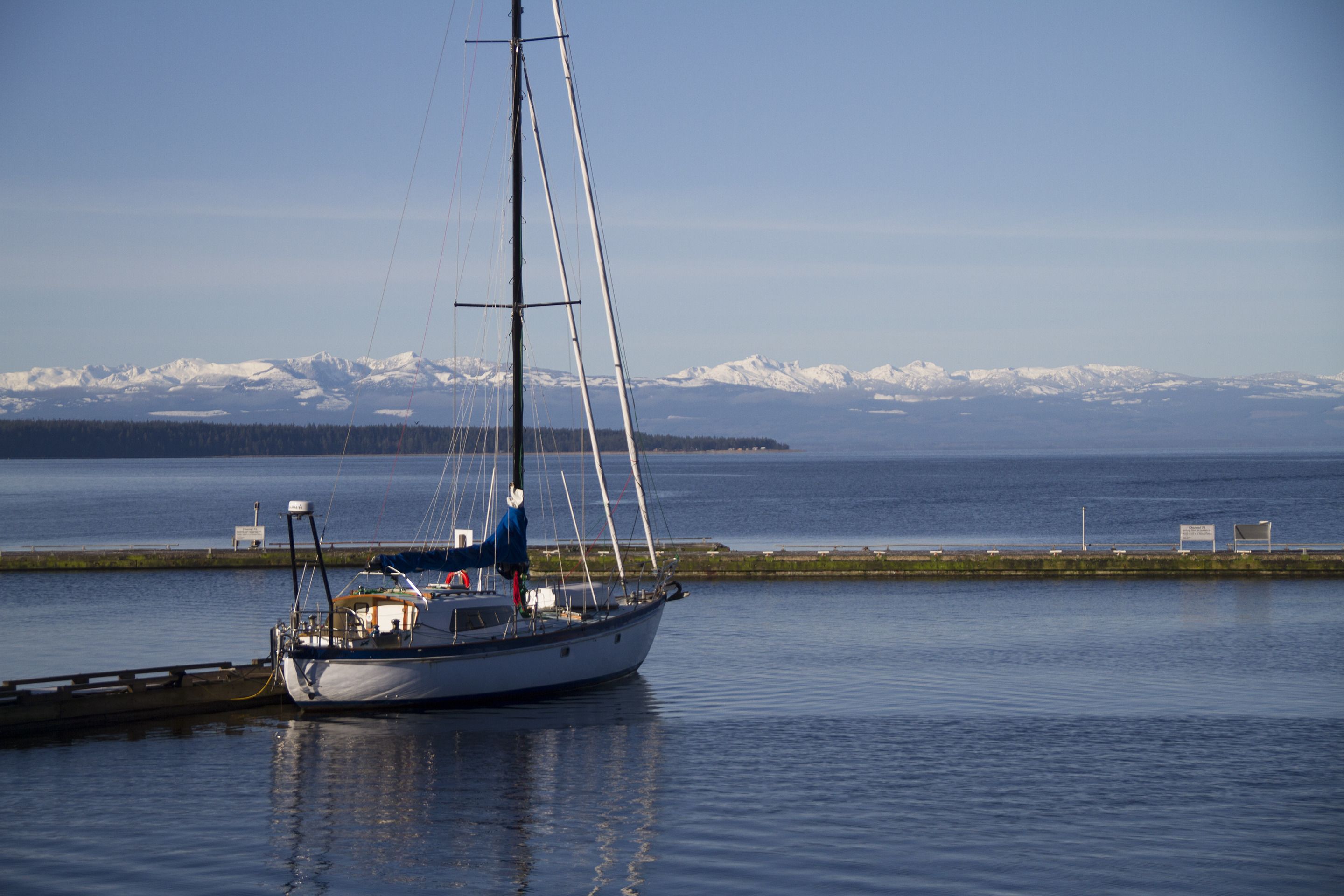 A sailboat docked near a calm body of water with a mountainous landscape in the background.