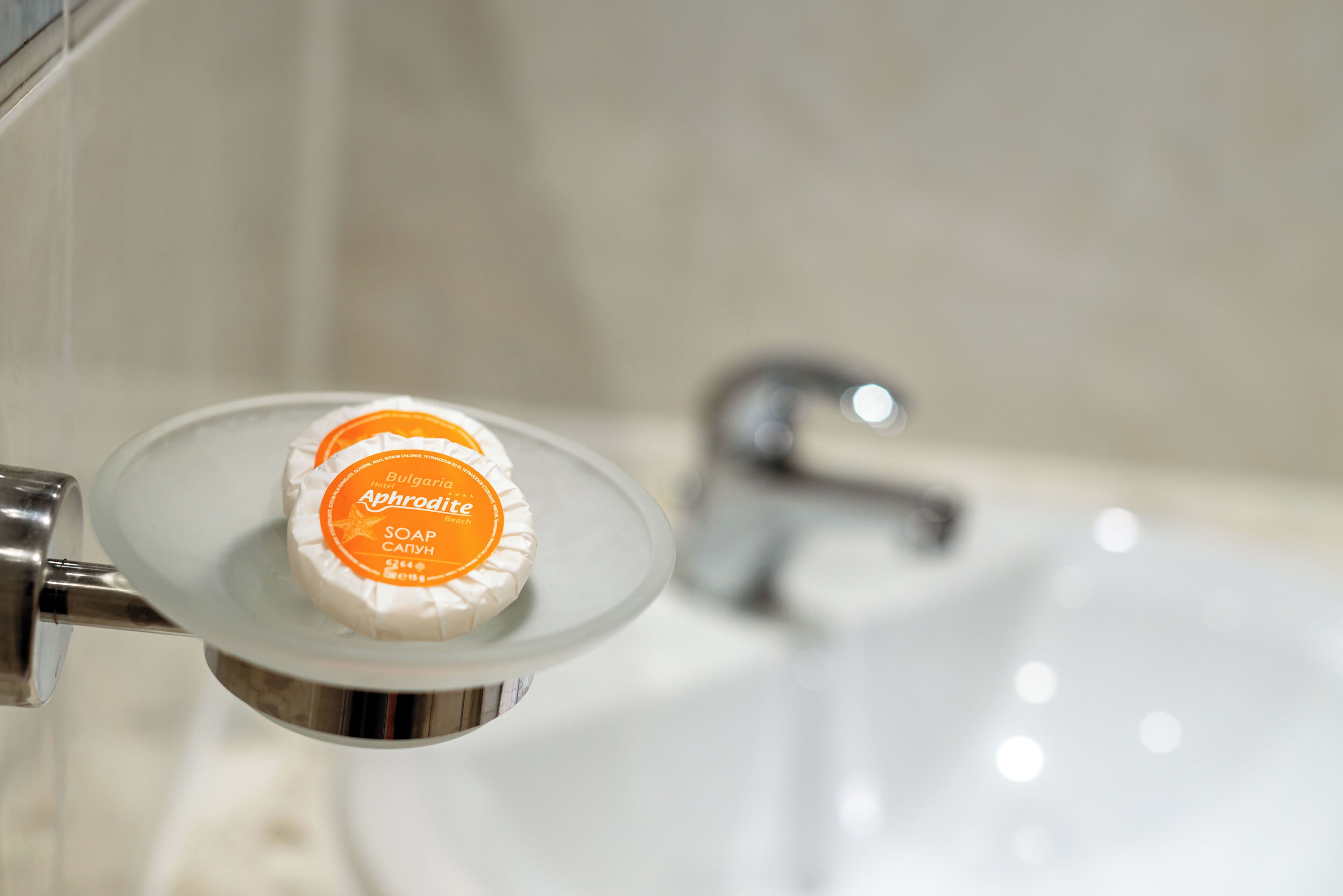 Un morceau de savon sur une petite assiette en verre, posé dans le lavabo d’une salle de bain.