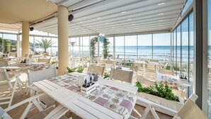 Un área de comedor al aire libre con mesas y sillas, con vista al mar.