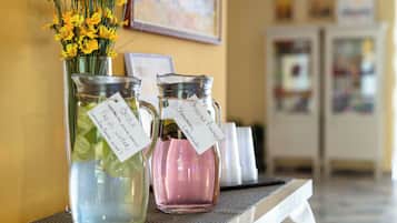 Dos botellas de vidrio con etiquetas, una con flores amarillas y la otra con líquido rosado, sobre una mesa en una habitación con pared amarilla y un refrigerador al fondo.