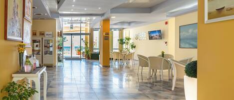 A hotel lobby with a marble floor, a reception desk, chairs, and framed artwork on the walls.