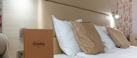 A neatly made bed with white and beige pillows, a brown hotel brochure on the nightstand, and a wall-mounted light fixture.