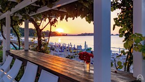 Una terraza con vistas a la puesta de sol sobre una playa con sombrillas y sillones de descanso.