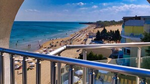 Vista al mar desde un balcón con barandilla, sombrillas de playa y cielo despejado.
