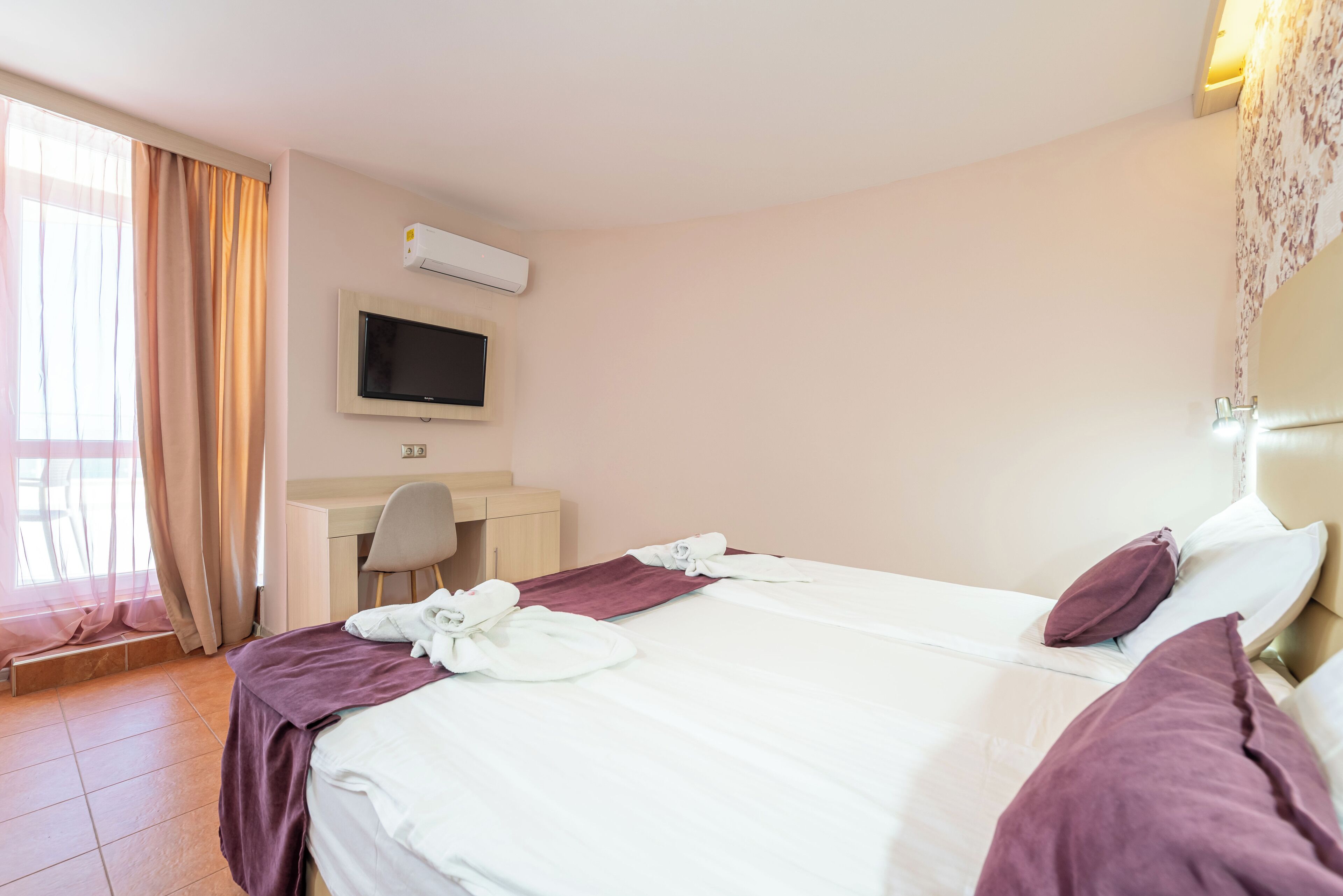 Ein Hotelzimmer mit Bett, Schreibtisch, Stuhl, Fernseher und einem Fenster mit Vorhängen.