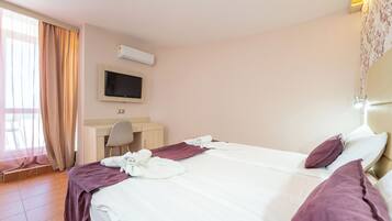 Ein Hotelzimmer mit Bett, Schreibtisch, Stuhl, Fernseher und einem Fenster mit Vorhängen.