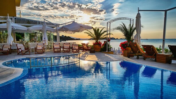 Zona junto a la piscina con sillones de descanso, sombrillas y vista al mar al atardecer.