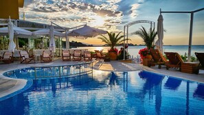 A poolside area with lounge chairs, umbrellas, and a view of the sea at sunset. - Aphrodite Beach Hotel (Nessebar)