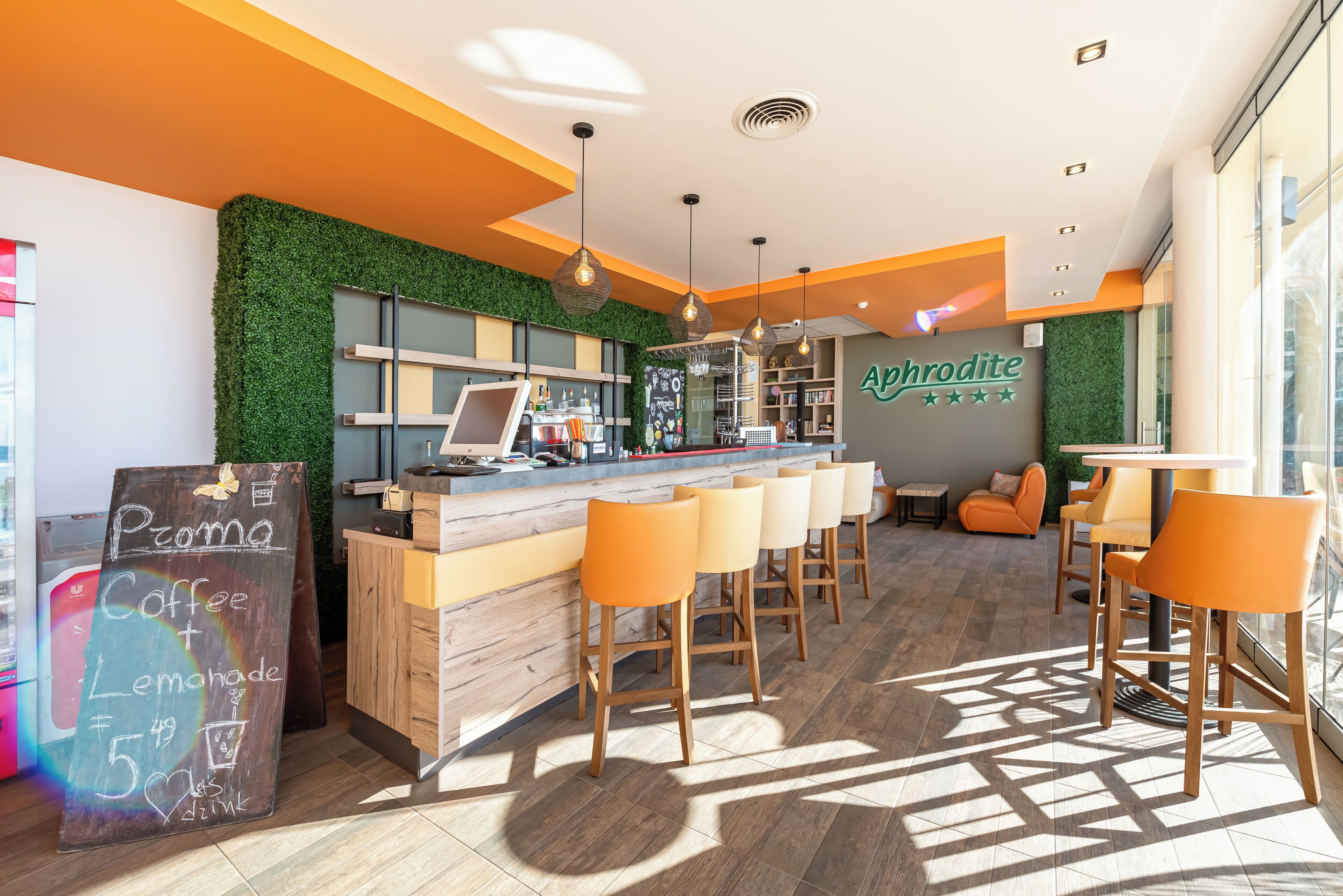 A modern coffee shop interior with a bar area, wooden stools, and a green wall.