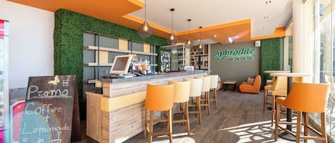 A modern coffee shop interior with a bar area, wooden stools, and a green wall.