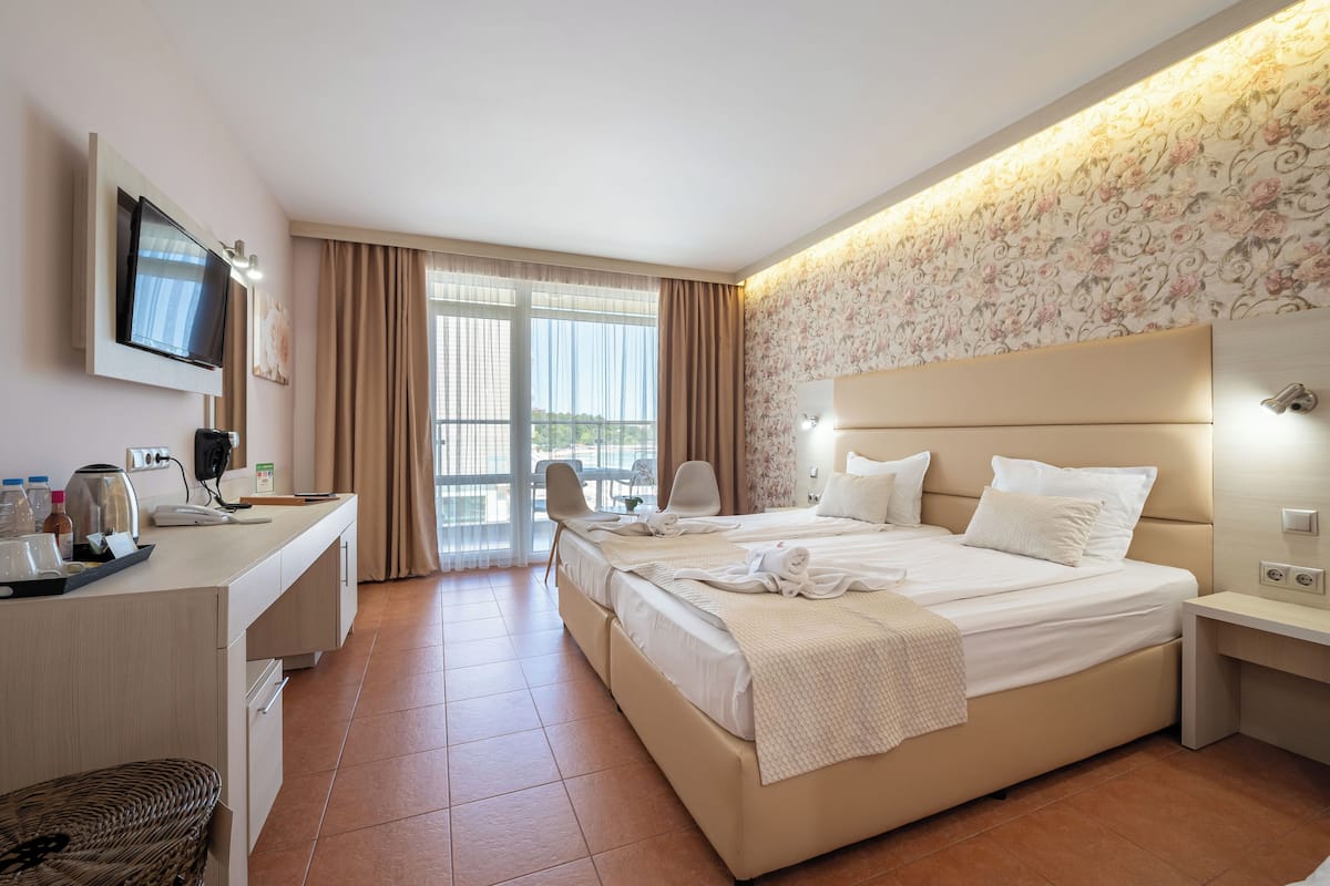 A hotel room with a large bed, a desk with a flat-screen TV, a chair, and a window with curtains.