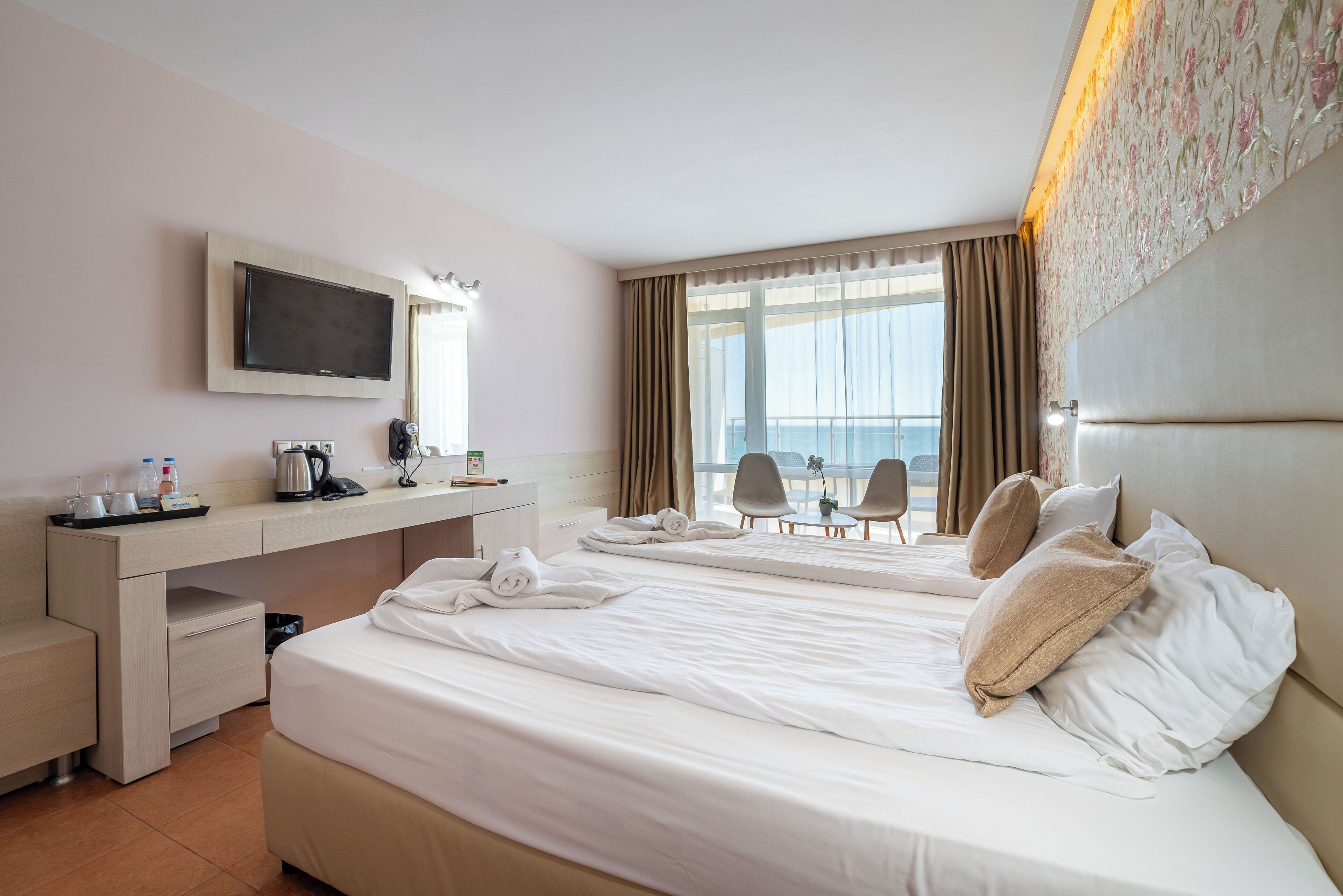 Quarto de hotel com duas camas, uma escrivaninha, televisão e vista para o mar.